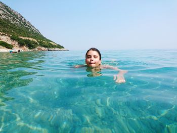 Boy swimming in sea against clear sky