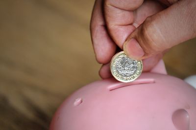 Close-up of hand holding coin over piggy bank