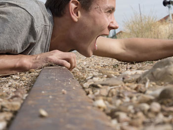 Close-up of man shouting while lying on railroad track