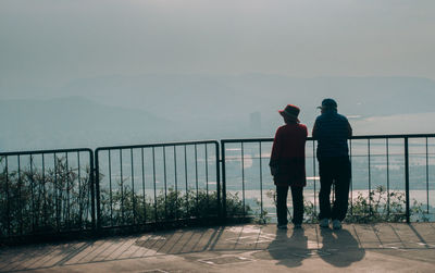 Rear view of man and woman standing by railing against sky