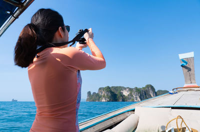 Young asian woman weraing swimsuit using camera to take photo while travel on long tail boat 