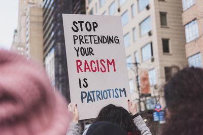 Close-up of hand with text against buildings in city, protest sign 