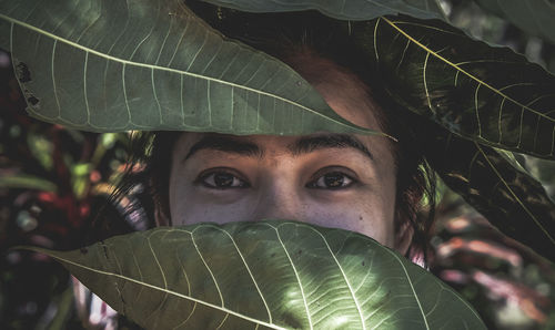 Close-up portrait of young woman with green leaves