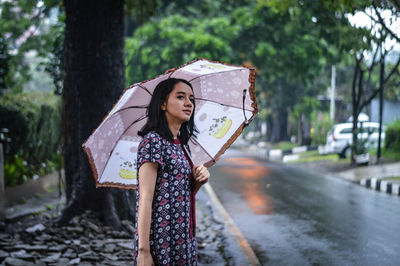 Young woman holding umbrella while standing on roadside