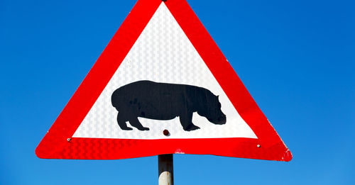 Low angle view of road sign against clear blue sky