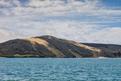 Scenic view of sea by mountain against sky