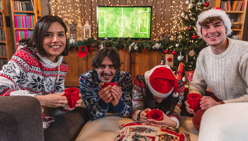 Group of four young friends toasting with red cups dressed in red hats and christmas sweatshirts