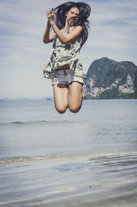 Young woman jumping at beach against sky