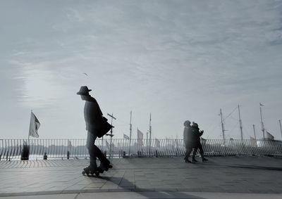 Rear view of men walking by sea against sky