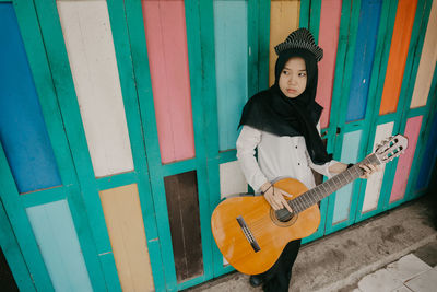 Full length of thoughtful woman playing guitar against wall