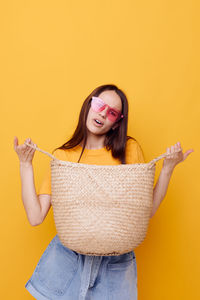 Portrait of young woman wearing hat standing against yellow background