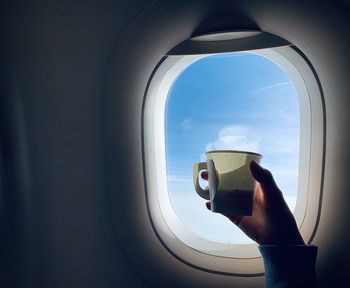 Close-up of person holding coffee by airplane window