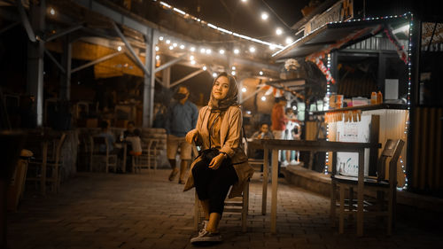 Full length of woman sitting by food stalls at night