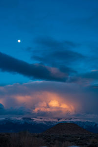 Scenic view of landscape at early sunrise with golden light in clouds and full moon in blue sky