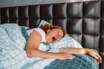 Woman yawning while lying on bed at home