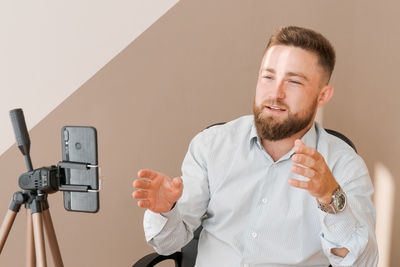 Smiling bearded business man, filming his video blog episode using smartphone