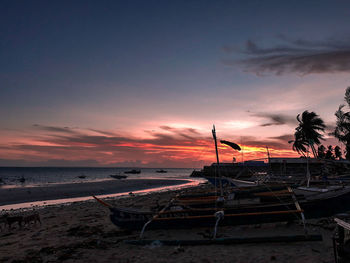 Boats moored on beach against sky during sunset