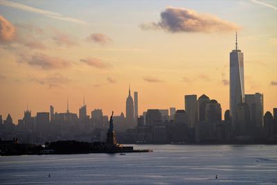 Statue of liberty and manhattan skyline against sky during sunset