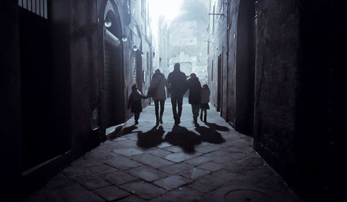 Rear view of silhouette people walking in alley amidst buildings in city