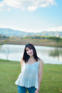 Portrait of young woman standing against lake