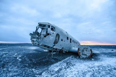 Abandoned boat on sea against sky during winter