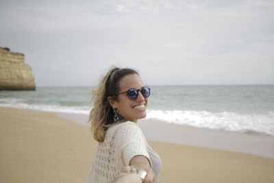 Portrait of smiling young woman standing at beach against sky