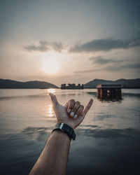 Midsection of person by sea against sky during sunset