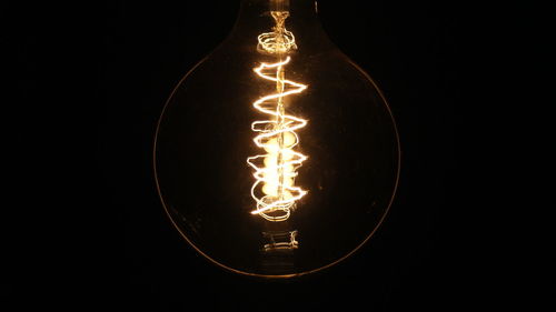 Close-up of illuminated light bulb against black background
