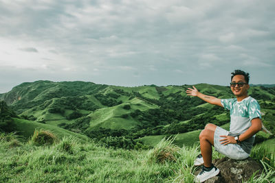 Full length of young man sitting on mountain against sky