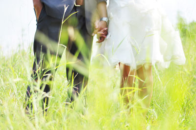 Midsection of bride and groom holding hands on grassy field