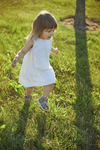 Charming child in linen dress walking on the lawn