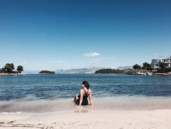 Rear view of woman sitting on shore against sea at beach