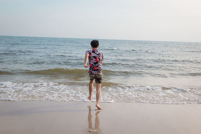 Rear view of boy on beach against sky