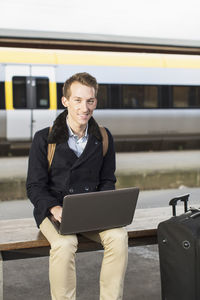 Portrait of happy young businessman using laptop on railroad station