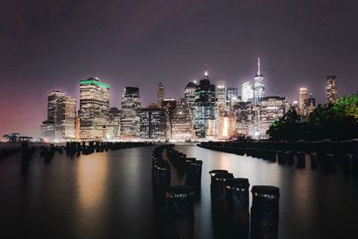 Illuminated buildings by river against sky in city at night