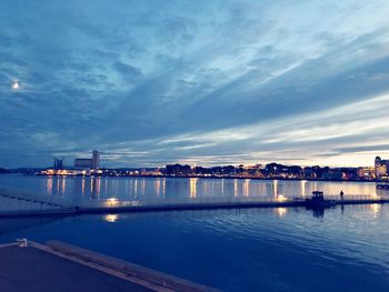 Sea by illuminated city against sky at dusk