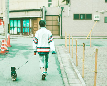 Rear view of man walking on street by building