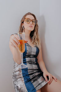 Portrait of young woman holding champagne flute against gray background