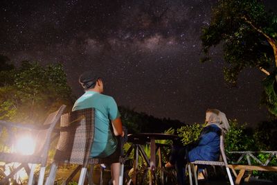 Rear view of man and woman standing against trees at night