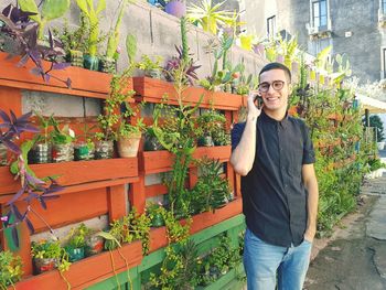 Young man talking on mobile phone while standing against potted plants