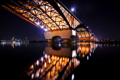 Illuminated bridge over river in city at night