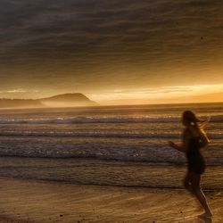 Woman walking on beach against sky during sunset