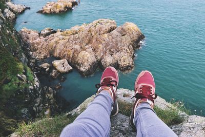 Low section of woman sitting on rock by sea