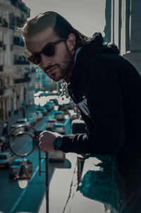 Side view of young man wearing sunglasses standing by railing in balcony