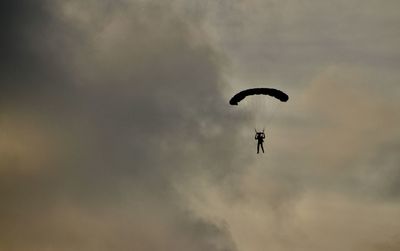 Low angle view of people paragliding against sky