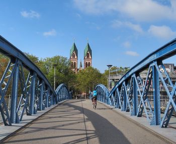 Rear view of biker on blue bridge with church steeples in background against sky