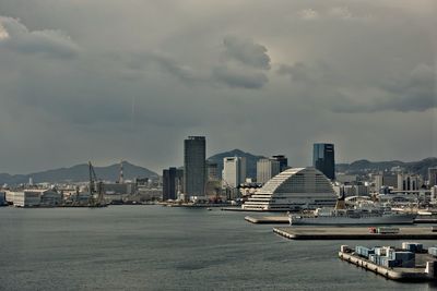 City at waterfront against cloudy sky