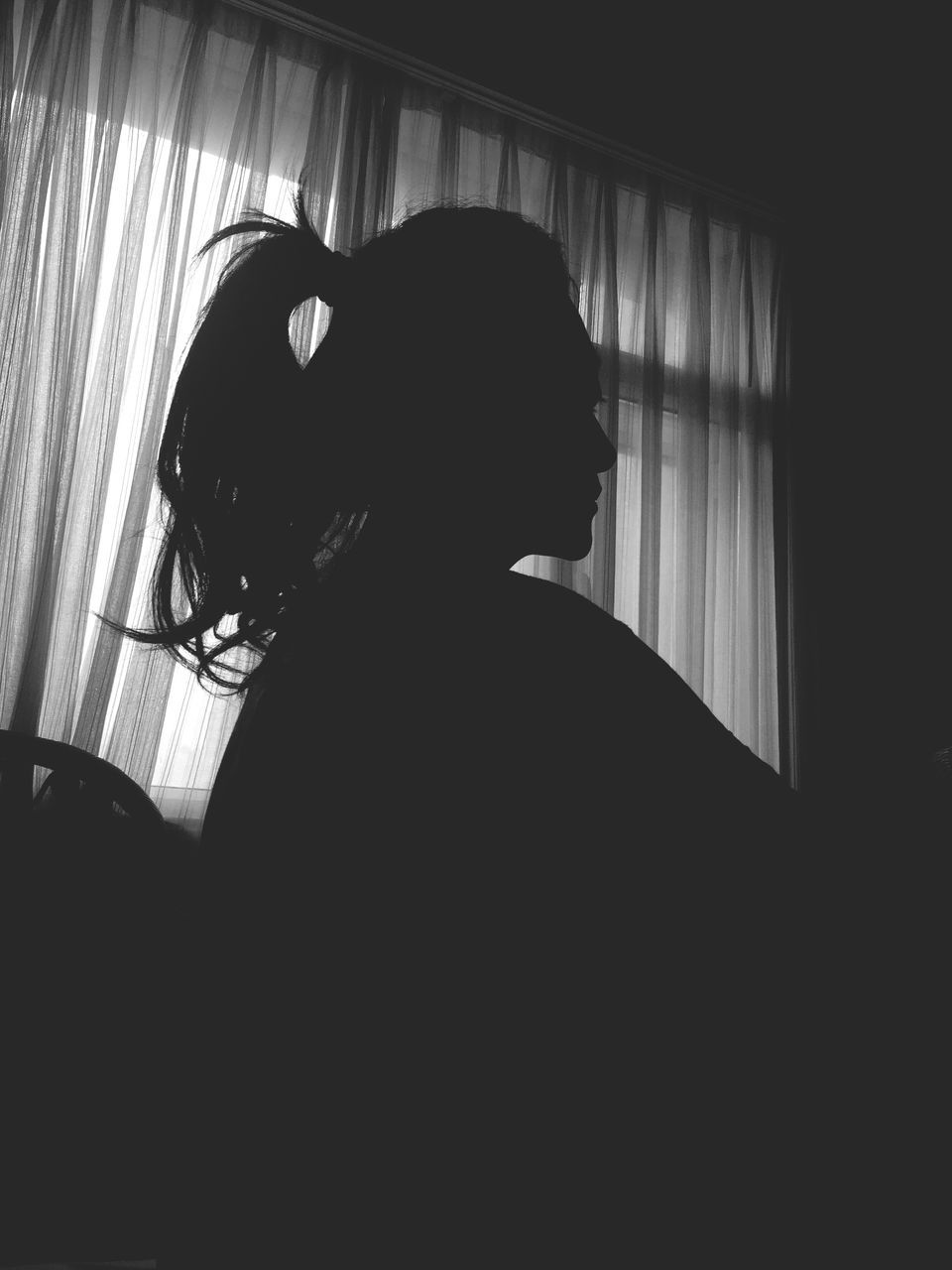 indoors, lifestyles, window, home interior, leisure activity, young adult, silhouette, contemplation, young women, curtain, dark, domestic room, side view, person, standing, wall - building feature, waist up, three quarter length