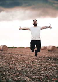 Full length of young man jumping on land against sky