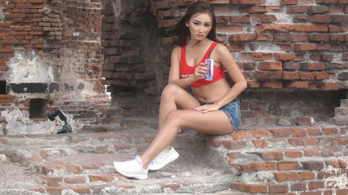 Portrait of young woman sitting against brick wall